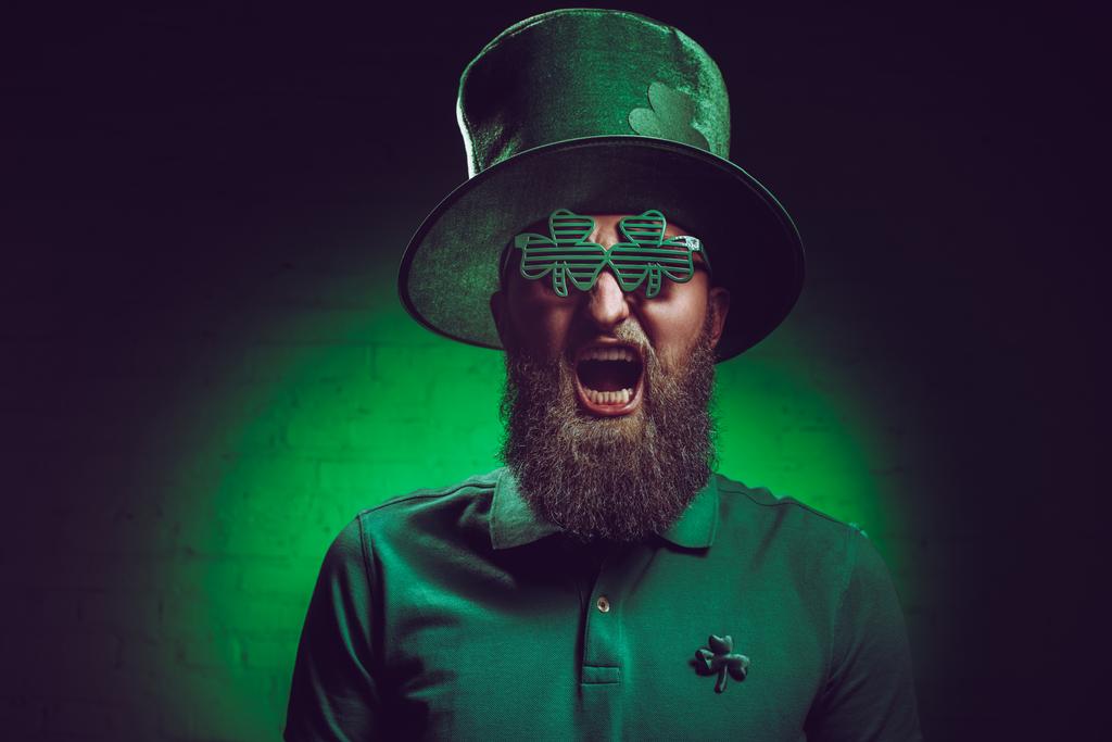 γενειοφόρος άνδρας σε πράσινο ιρλανδικό καπέλο και αστεία γυαλιά ουρλιάζοντας σε κάμερα - Φωτογραφία, εικόνα