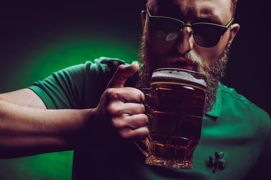 parrakas mies aurinkolasit ja vihreä poolopaita juo olutta
 - Valokuva, kuva
