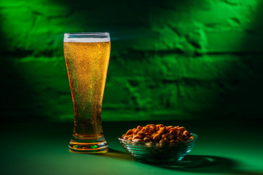 Nahaufnahme des Glases mit frischem kalten Bier und gesalzenen Erdnüssen auf dem Teller - Foto, Bild