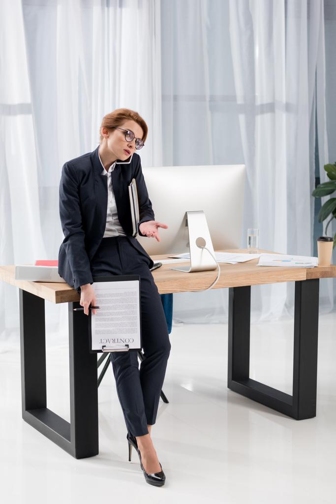 Geschäftsfrau mit Dokumenten spricht im Büro auf Smartphone - Foto, Bild