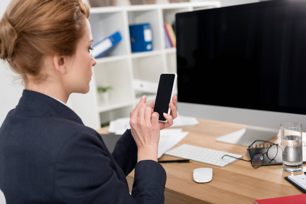 boční pohled podnikatelka v obleku pomocí smartphone na pracovišti v úřadu - Fotografie, Obrázek