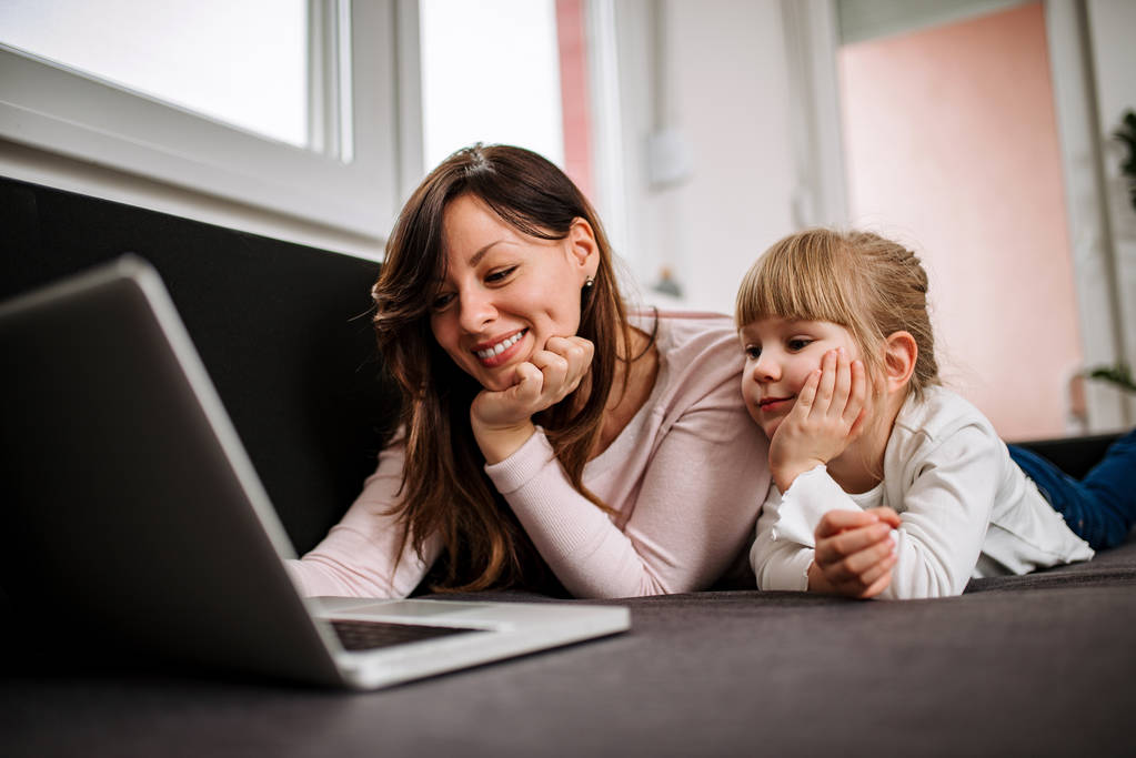 junge Mutter und Tochter sehen Bilder am Laptop zu Hause. - Foto, Bild