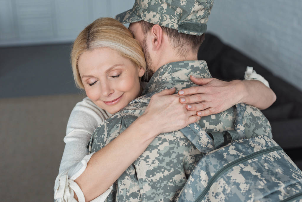 gülümseyen anne sarılma yetişkin oğlu evde askeri üniformalı - Fotoğraf, Görsel