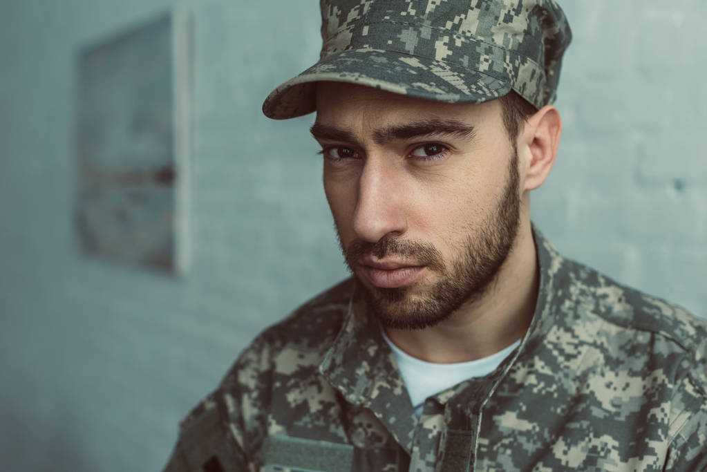retrato de soldado em uniforme militar olhando para câmera contra parede de tijolo branco
 - Foto, Imagem