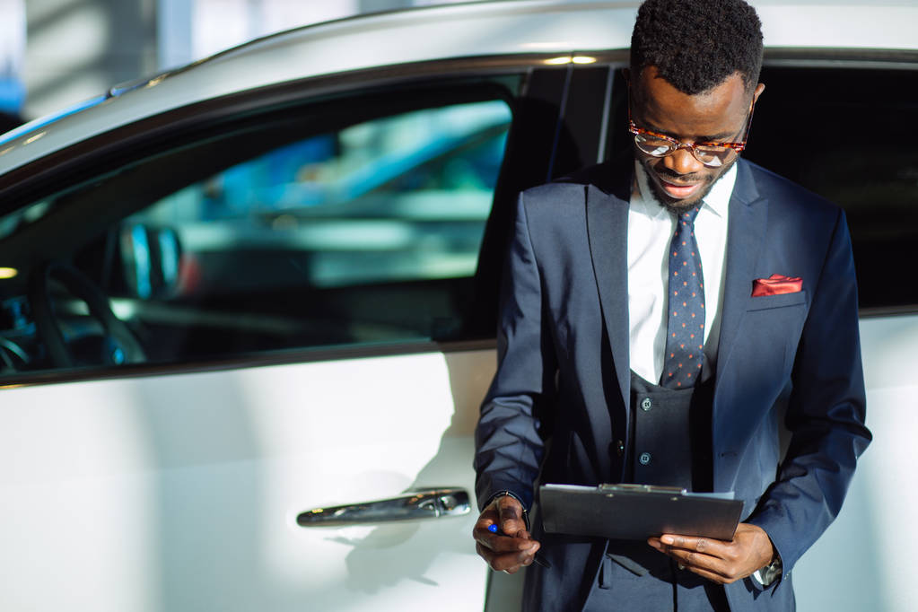 Handsome african car salesman standing at the dealership holding a tablet - Photo, Image
