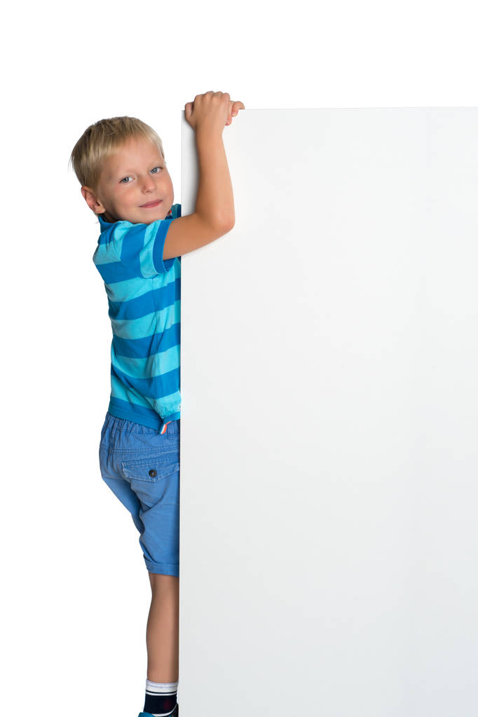 Un petit garçon regarde par derrière une bannière vide. - Photo, image
