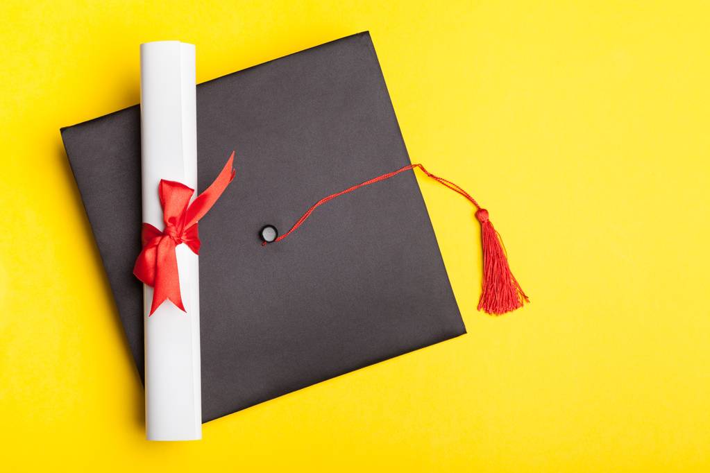 Chapéu de graduação e diploma em fundo amarelo
  - Foto, Imagem
