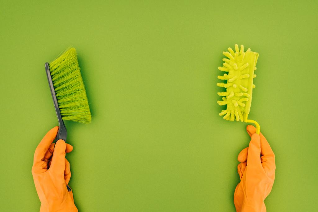 abgeschnittenes Bild einer Frau, die zwei verschiedene Putzbürsten in den Händen hält, isoliert auf grün - Foto, Bild