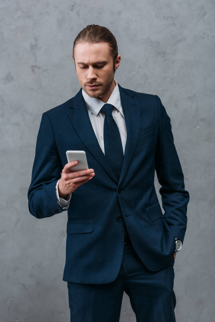 hombre de negocios guapo y seguro usando un teléfono inteligente frente a la pared de hormigón
 - Foto, Imagen