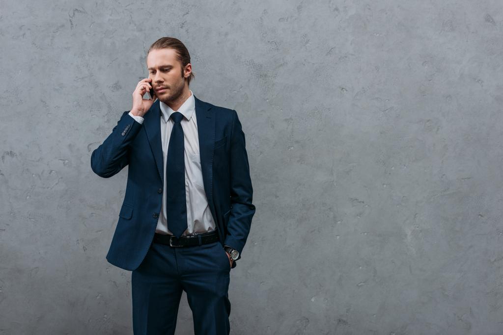 серйозний красивий бізнесмен розмовляє по телефону перед бетонною стіною
 - Фото, зображення