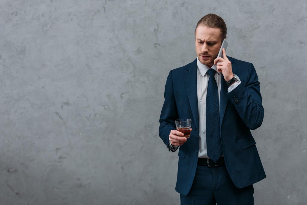 Молодой серьезный бизнесмен со стаканом виски разговаривает по телефону
 - Фото, изображение