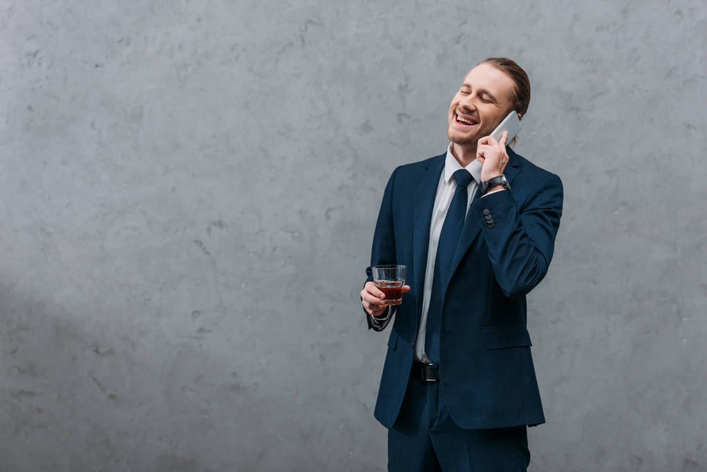 młody biznesmen roześmiany z szklankę whisky, rozmawiając przez telefon - Zdjęcie, obraz