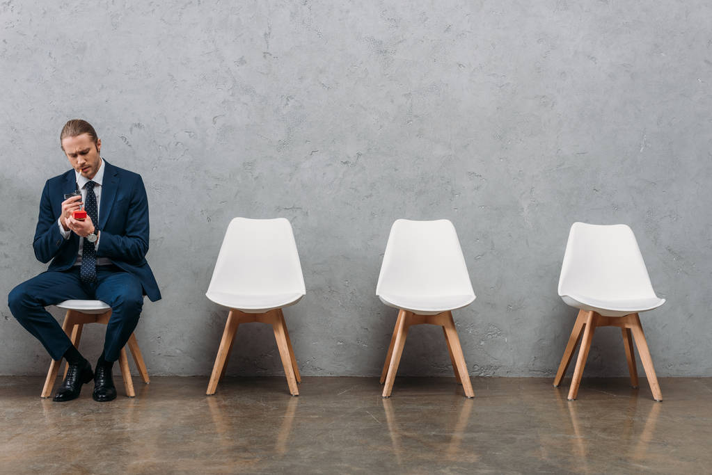 einsamer Geschäftsmann sitzt auf Stuhl und raucht vor Betonwand - Foto, Bild