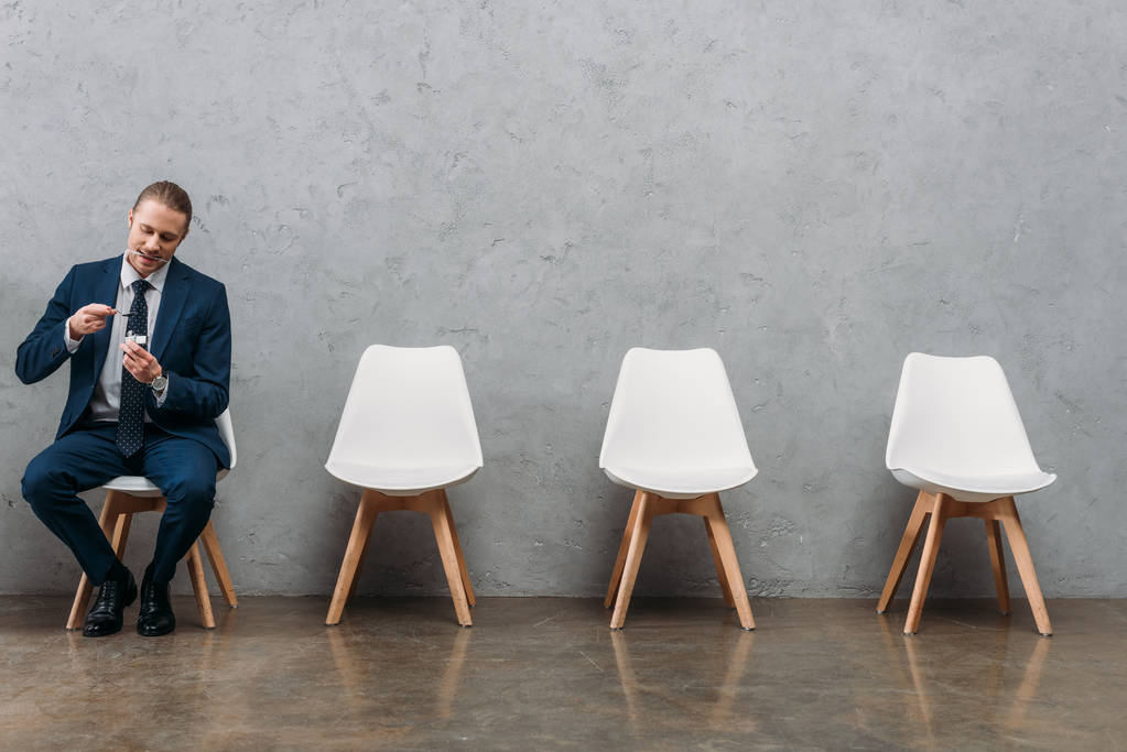 одинокий бизнесмен, кипящий героин в ложке, сидя на стуле под бетонной стеной
 - Фото, изображение