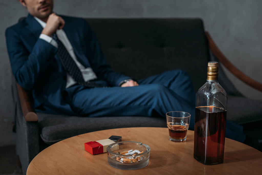 cropped shot of businessman sitting on couch in front of table with bottle of whiskey - Photo, Image