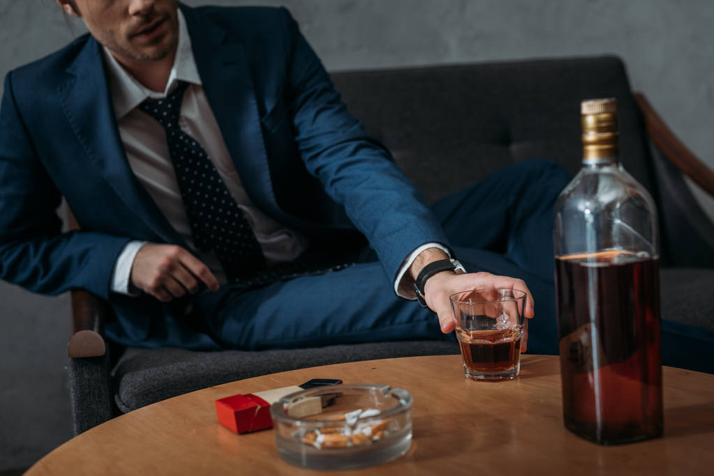 colpo ritagliato di uomo d'affari che prende un bicchiere di whisky dal tavolo
 - Foto, immagini