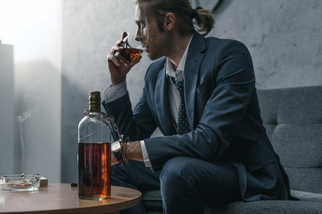alkohol rabja üzletember, üveg- és üveg whiskyt a kanapén ül - Fotó, kép