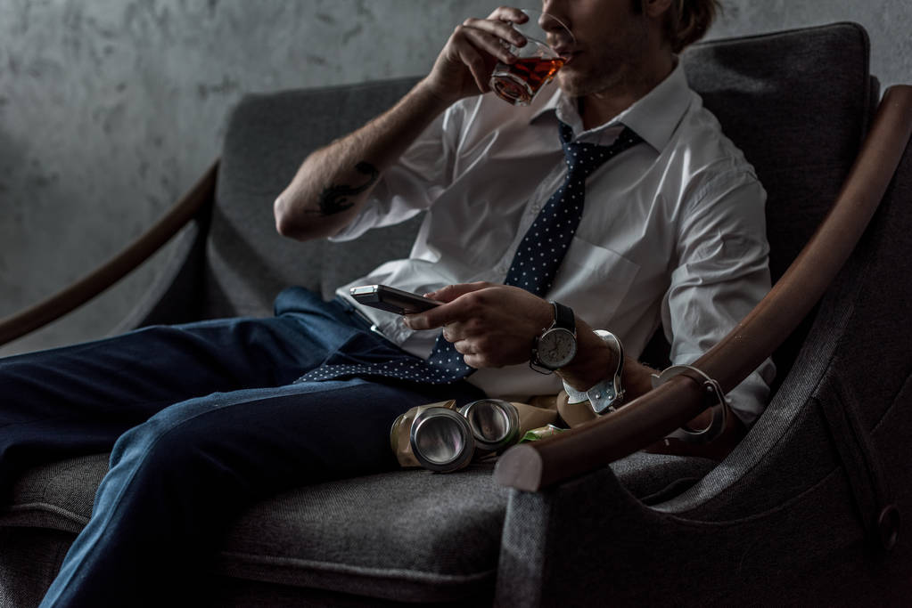 oříznutý snímek alkoholu závislý muž v bílé košili, sledování televize a pití whisky po práci - Fotografie, Obrázek