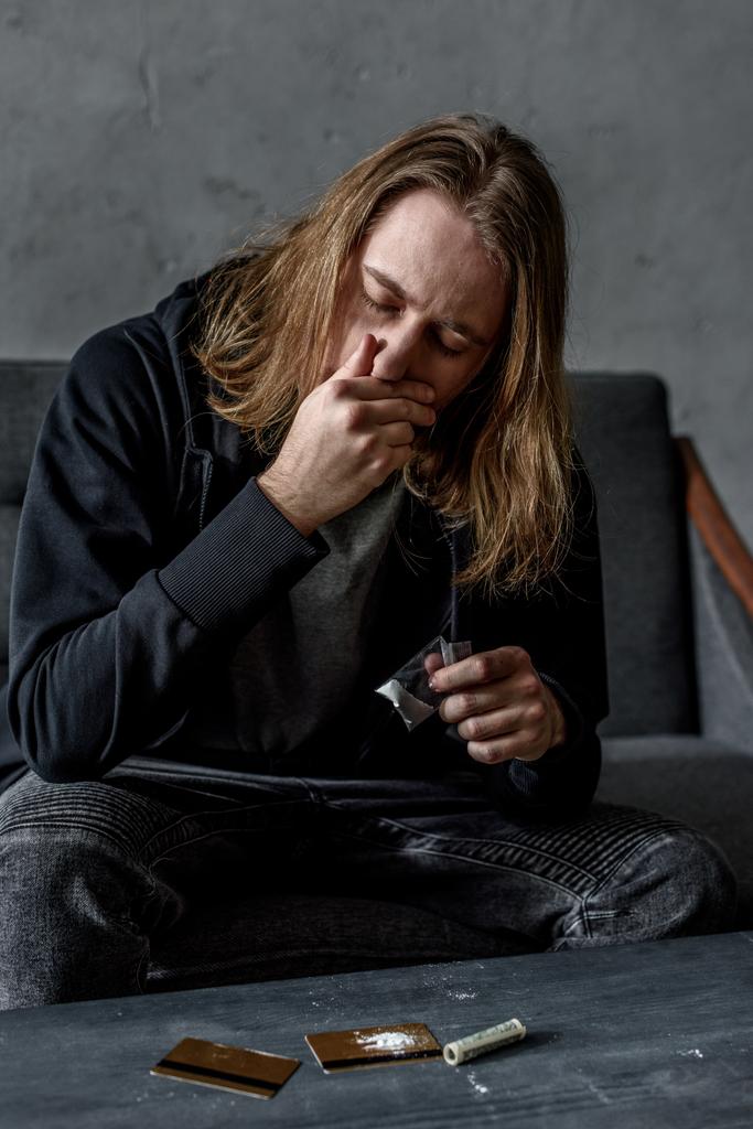 addicted man sniffing cocaine while sitting on couch - Photo, Image