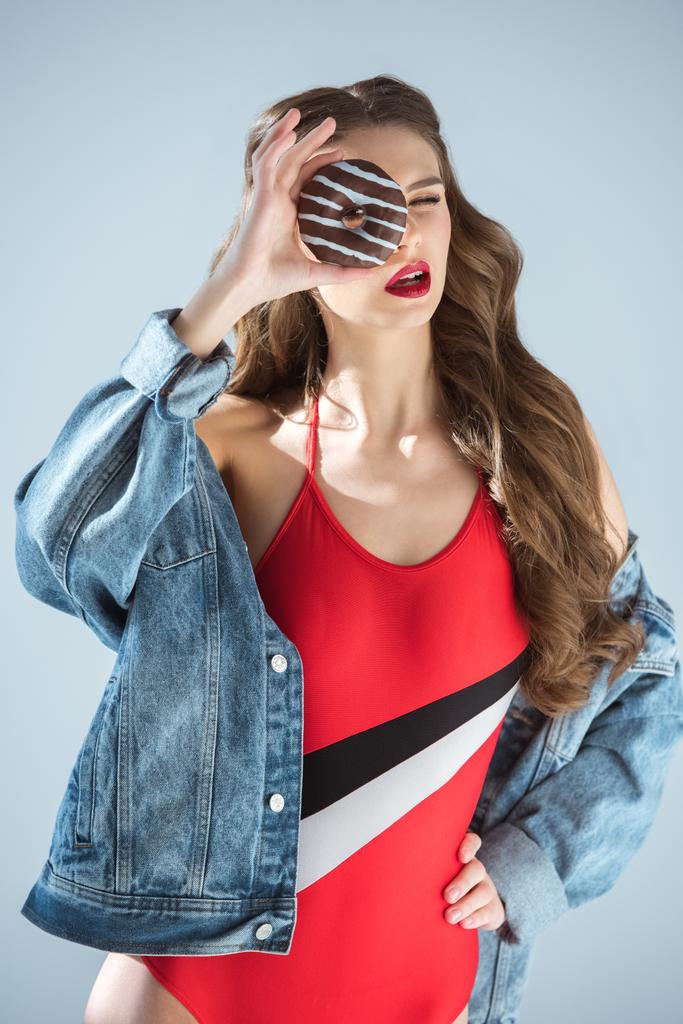 σέξι κορίτσι με κόκκινο μαγιό που ψάχνετε μέσω ντόνατ που απομονώνονται σε γκρι - Φωτογραφία, εικόνα
