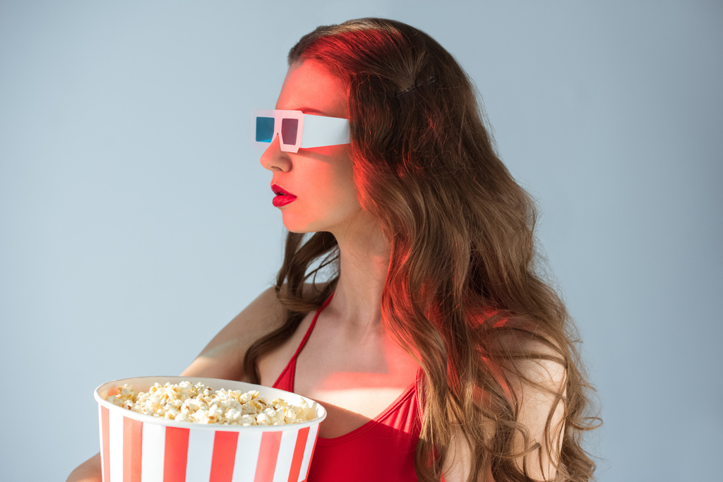 boční pohled svůdné dívky v 3d brýlích držení popcornu izolovaných na šedá - Fotografie, Obrázek