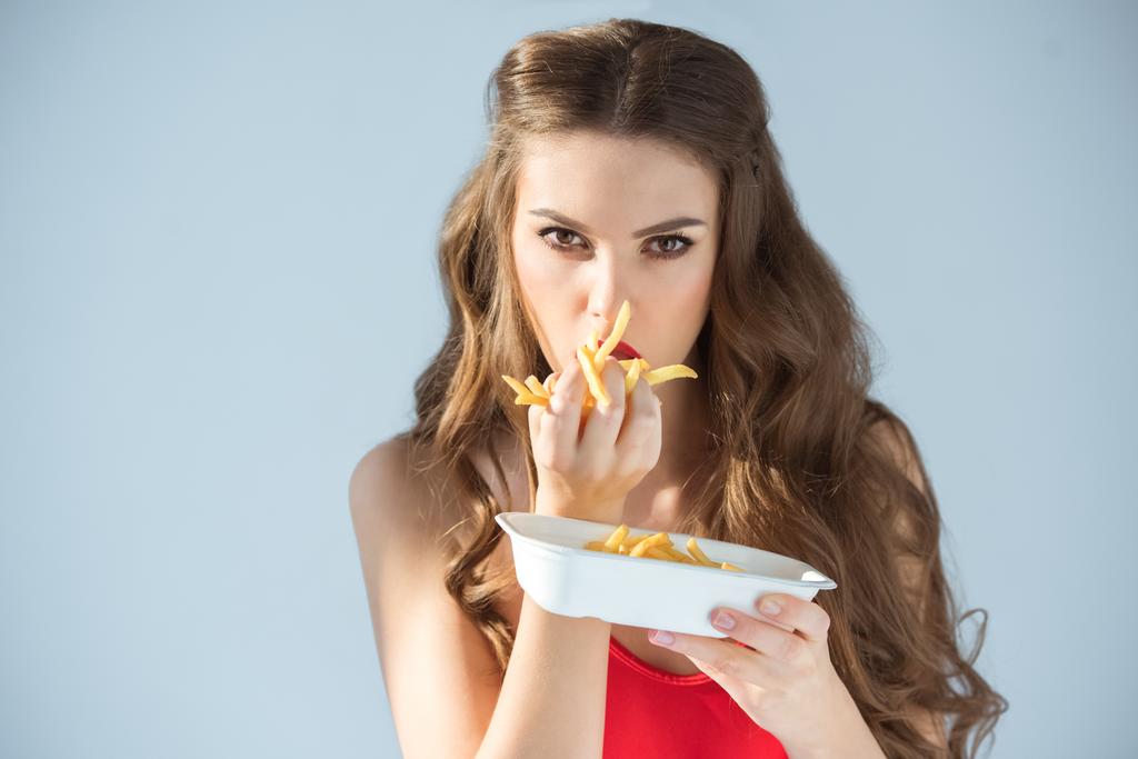 Seksikäs tyttö punainen uimapuku syö ranskalaisia perunoita eristetty harmaa
 - Valokuva, kuva