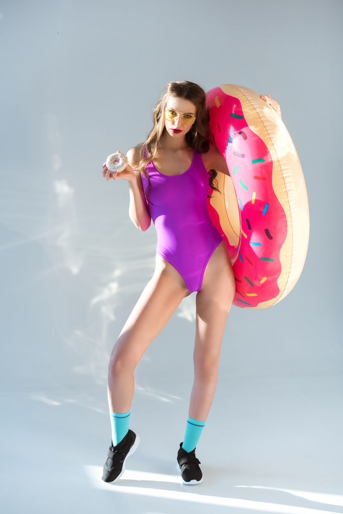 sexy attractive girl in ultra violet swimsuit holding donut and inflatable donut on grey - Photo, Image