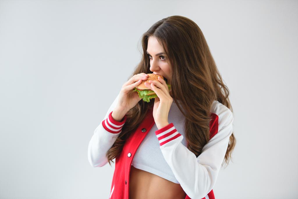 uwodzicielski dziewczyna w baseball kurtka jedzenie na białym tle burger - Zdjęcie, obraz
