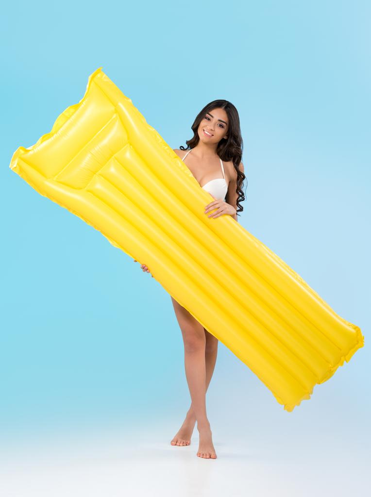beautiful young woman posing with yellow inflatable mattress, isolated on blue - Photo, Image