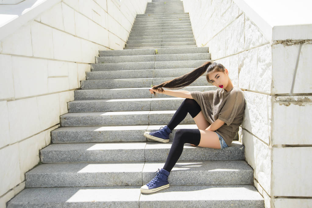 divertido asiático chica con largo negro cabello sentado en la escaleras
 - Foto, Imagen