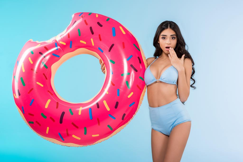 ελκυστική κοπέλα σοκαρισμένος με φουσκωτό ντόνατ δαχτυλίδι, απομονώνονται σε μπλε  - Φωτογραφία, εικόνα