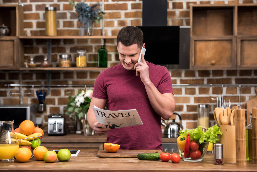 šťastný mladý muž mluví o smartphone a čtenářský deník cestování v kuchyni - Fotografie, Obrázek