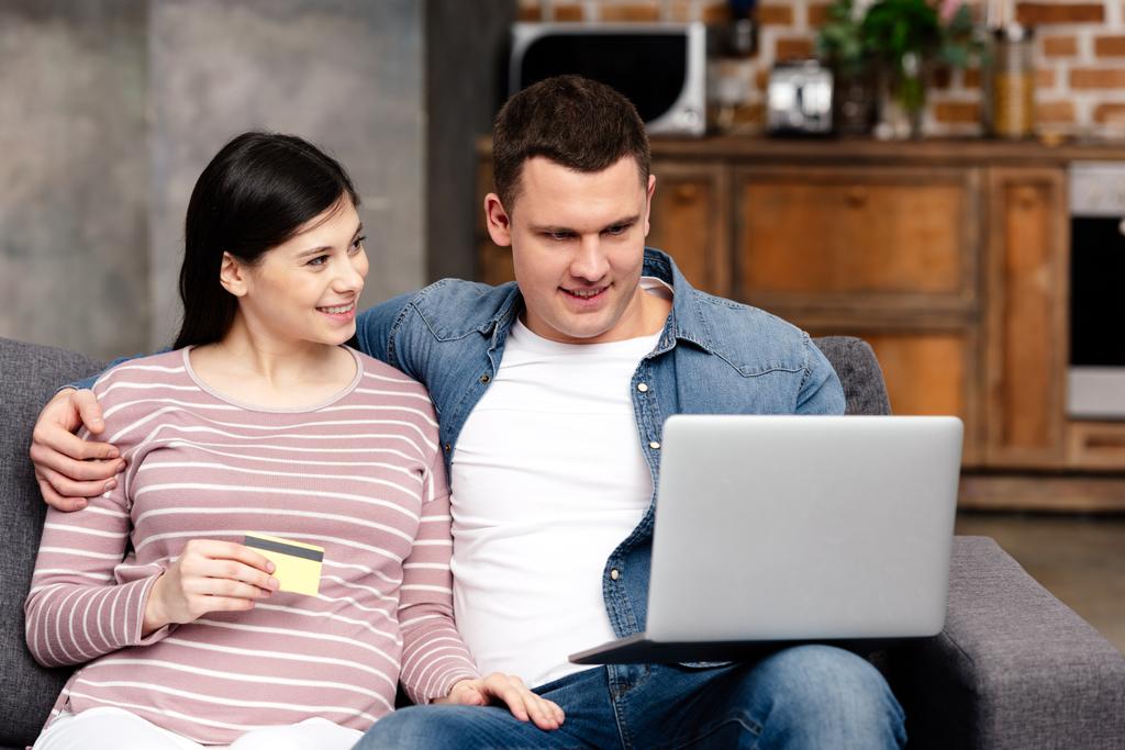 heureux jeune couple enceinte avec carte de crédit en utilisant ordinateur portable ensemble à la maison
 - Photo, image