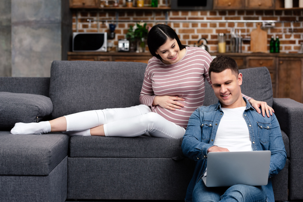 feliz joven pareja embarazada utilizando el ordenador portátil en casa
 - Foto, Imagen