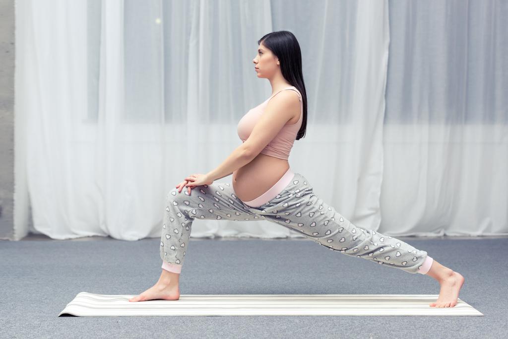 vista lateral da jovem grávida praticando ioga em casa
  - Foto, Imagem