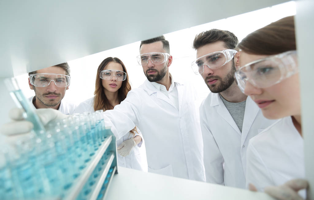 background image is a group of microbiologists studying the liquid in the glass tube. - Photo, Image
