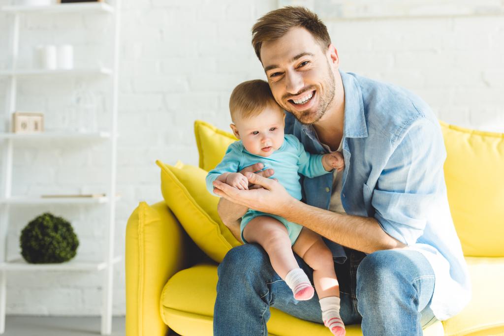 Giovane padre sorridente seduto sul divano con figlia in mano
 - Foto, immagini