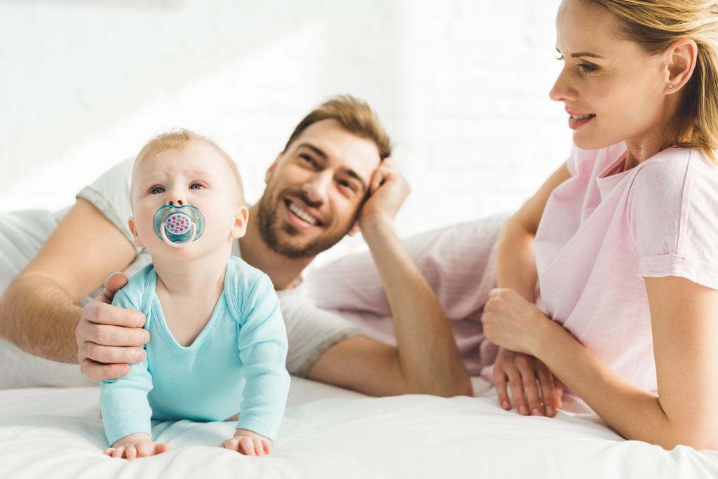 Genitori sorridenti e figlia neonata con manichino bambino a letto
 - Foto, immagini