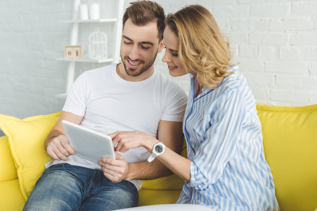 Smiling couple having fun with tablet and sitting on sofa - Photo, Image