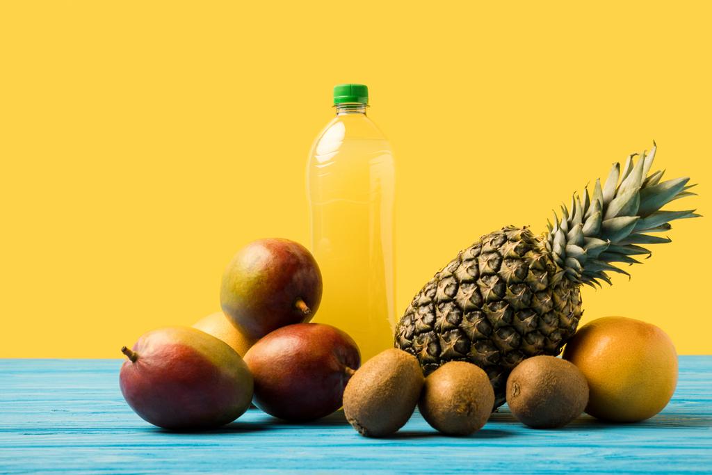 Turkuaz ahşap masa üzerinde plastik şişe taze olgun tropikal meyve ve doğal meyveli içecek - Fotoğraf, Görsel