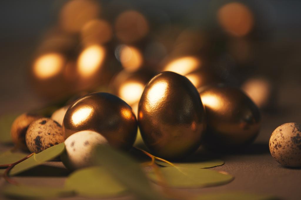 Закрыть пасхальные золотые яйца с листьями на столе
 - Фото, изображение