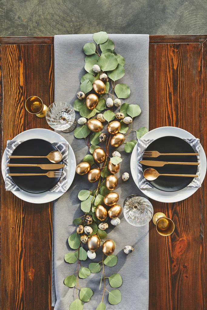 top view of easter golden eggs, plates and utensil on festive table in restaurant - Photo, Image