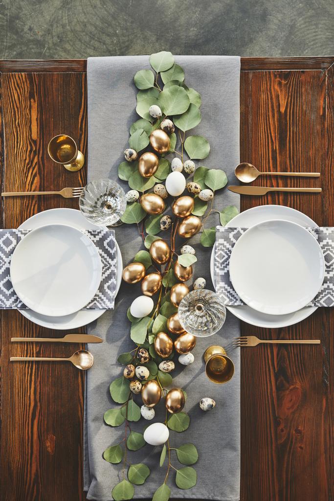 vista superior de ovos dourados de Páscoa, pratos e copos na mesa festiva no restaurante
 - Foto, Imagem