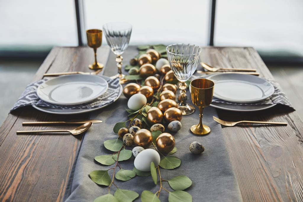 Goldene Ostereier, Teller und Gläser auf dem Tisch - Foto, Bild