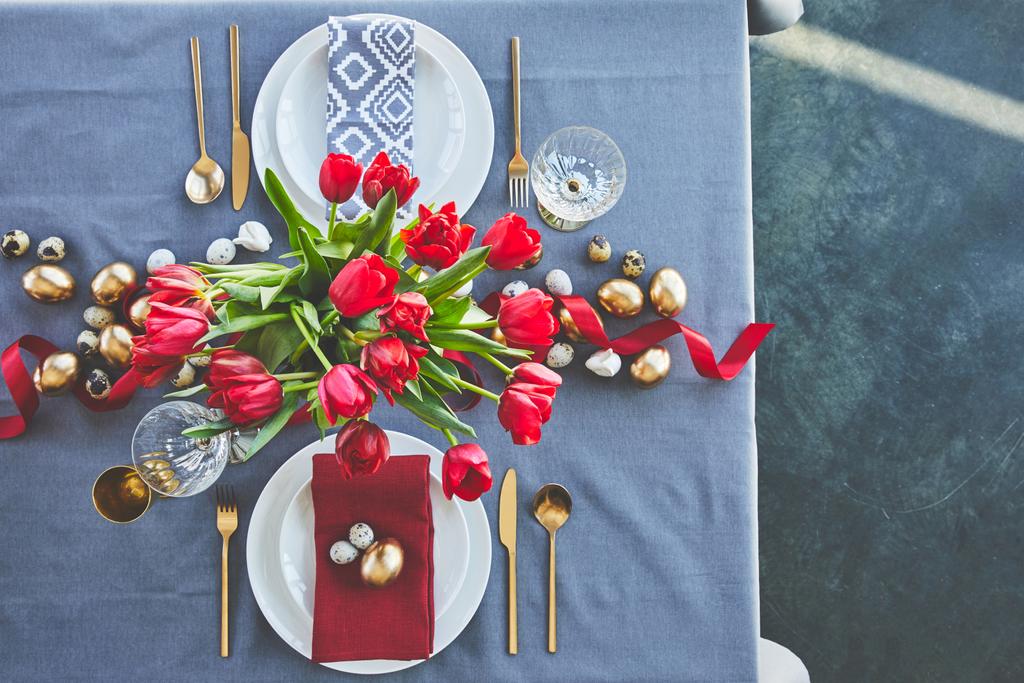 κάτοψη της ανθοδέσμης των κόκκινων τουλιπών και Πασχαλινά αυγά στο γιορτινό τραπέζι  - Φωτογραφία, εικόνα