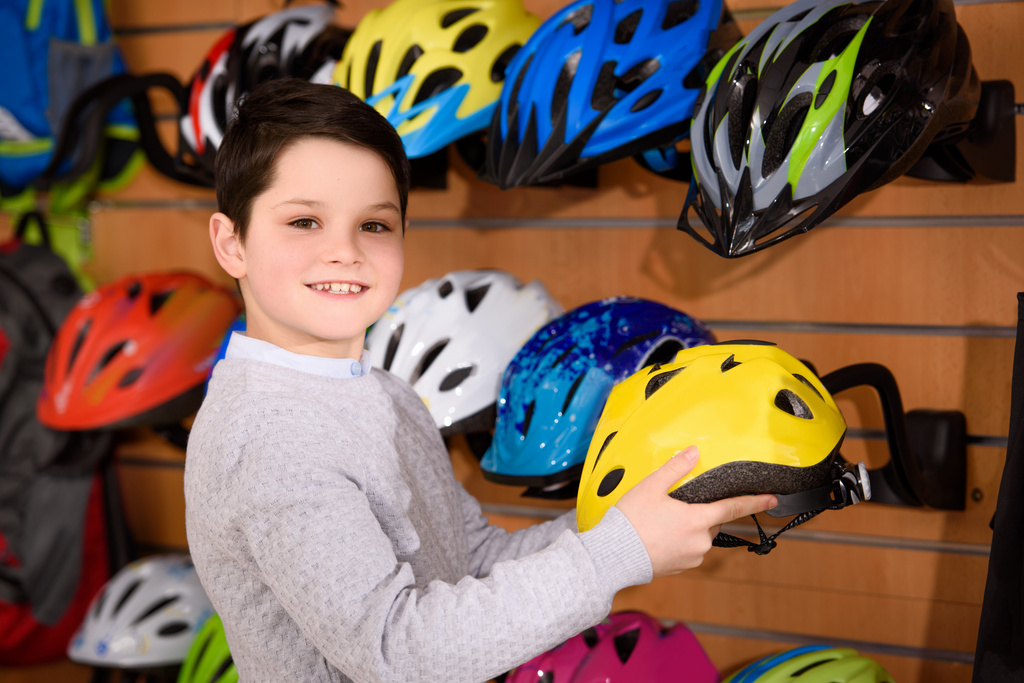 carino bambino che tiene il casco della bicicletta e sorride alla macchina fotografica nel negozio di biciclette
  - Foto, immagini