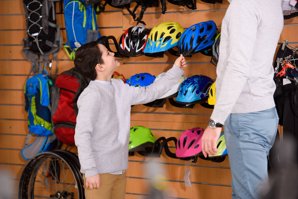 rajattu laukaus isä ja hymyilevä poika valitsemalla polkupyörän kypärät pyöräkaupassa
  - Valokuva, kuva