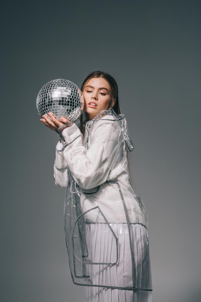 retrato de mujer joven en impermeable de moda con bola disco aislado en gris
 - Foto, Imagen
