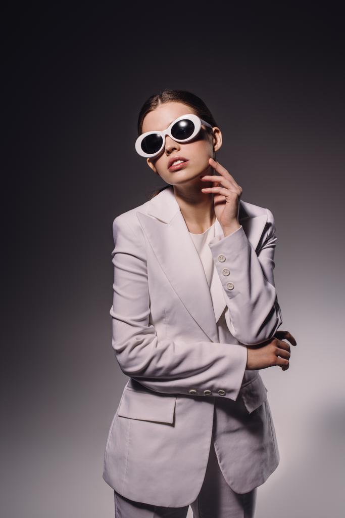 Portret van stijlvolle vrouw in wit pak en brillen poseren op donkere achtergrond - Foto, afbeelding