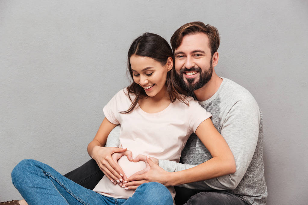 Χαμογελώντας όμορφος άνδρας με τη γυναίκα του έγκυος κάνει καρδιάς χειρονομία. - Φωτογραφία, εικόνα